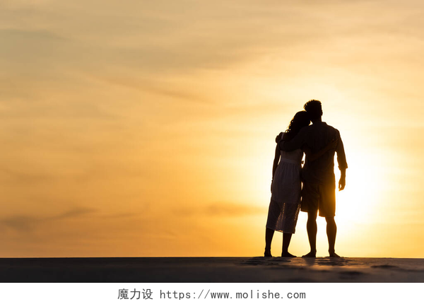 黄昏下站在沙滩上看日落的夫妻背影日落时分，男人和女人在海滩上拥抱阳光的轮廓